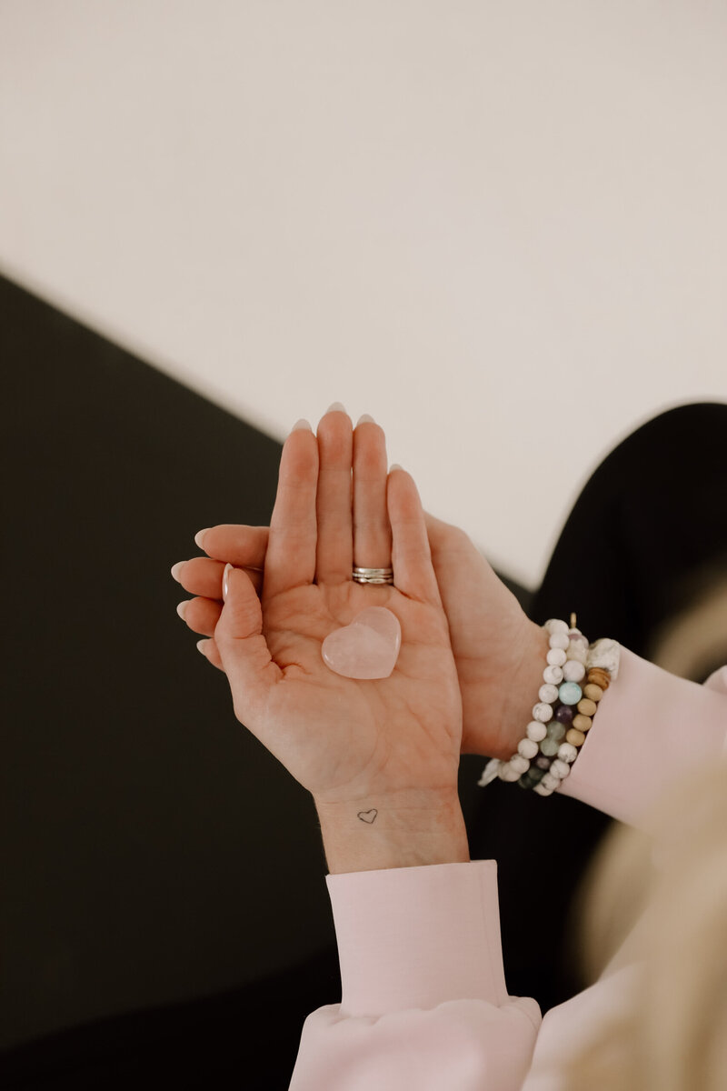 Hands that are overlapped and holding a pink heart crystal