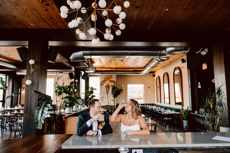 Bride and groom sitting at an empty bar drinking together