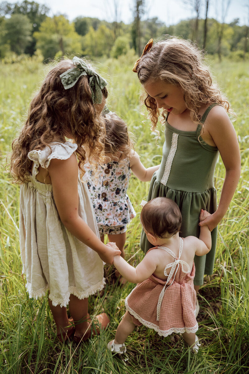 Four sisters holding hands and dancing in a field.
