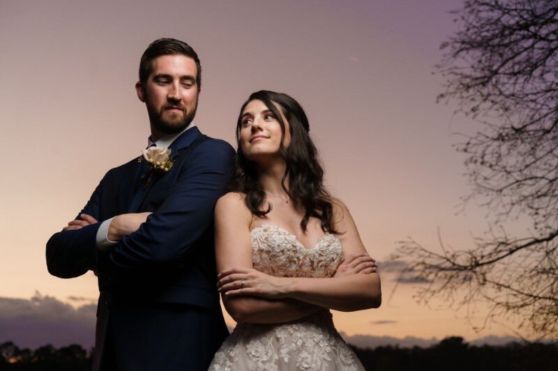 bride and groom lean on each other striking a dramatic pose with the sun setting in the background