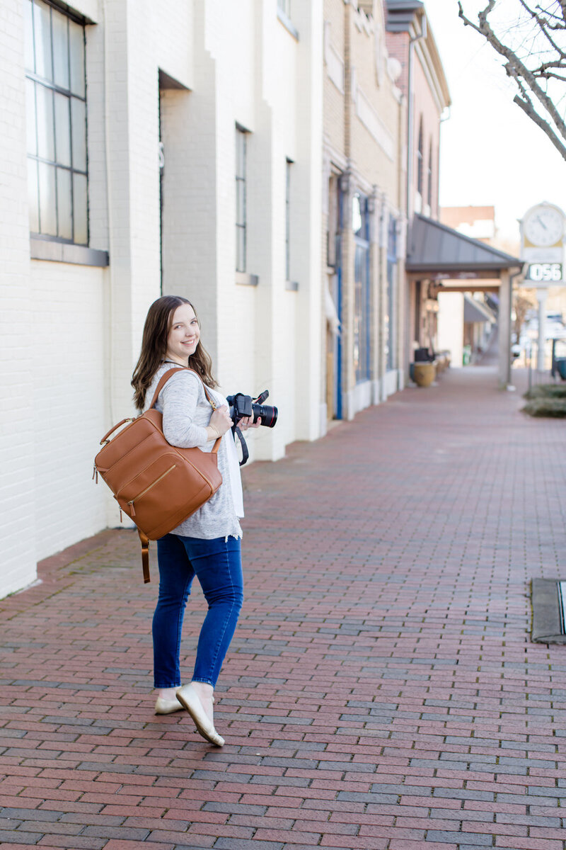 Photographer holds camera and walks down pathway in Downtown Buford