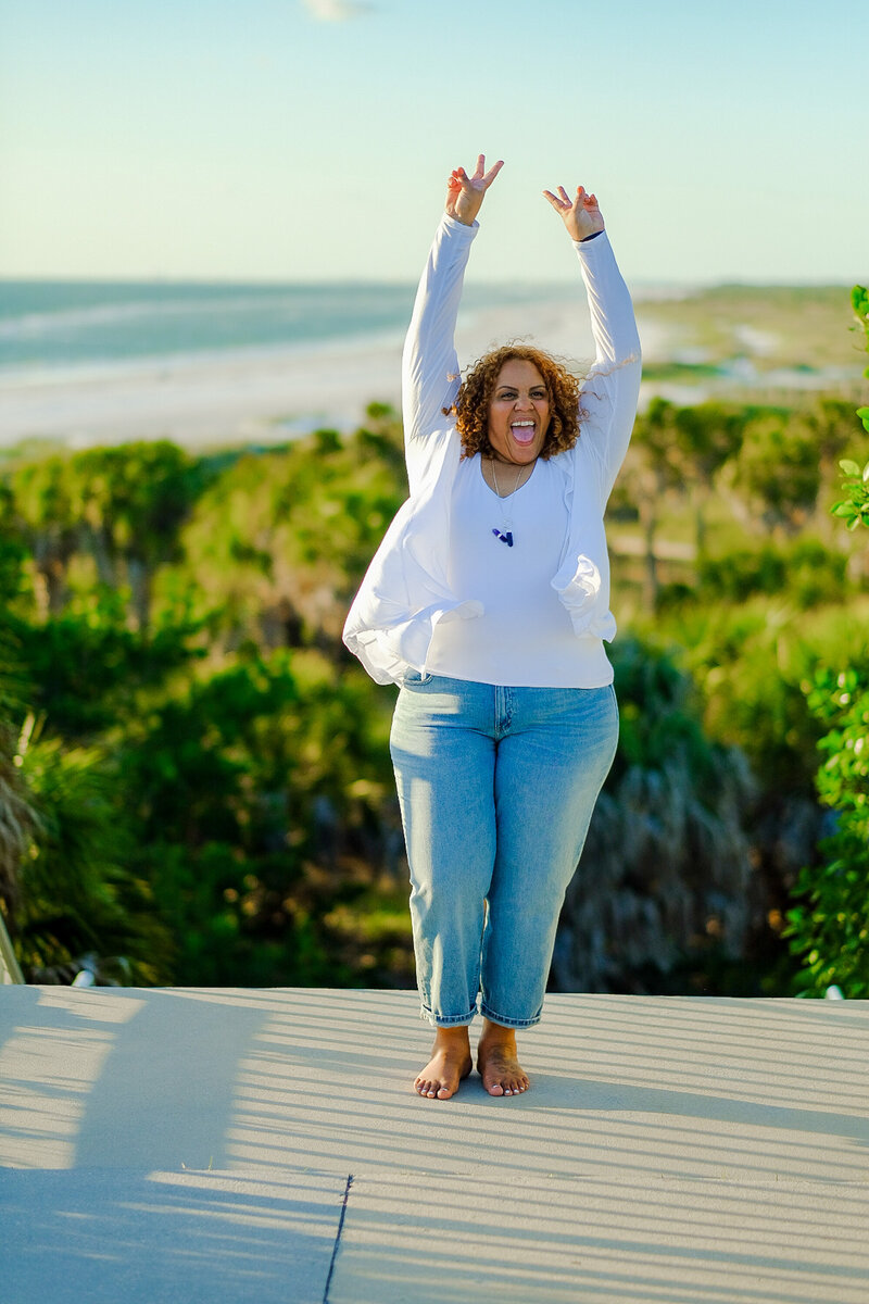 Certified life coach Claudine Martinell standing barefoot while raising hands showing joy and authenticity.