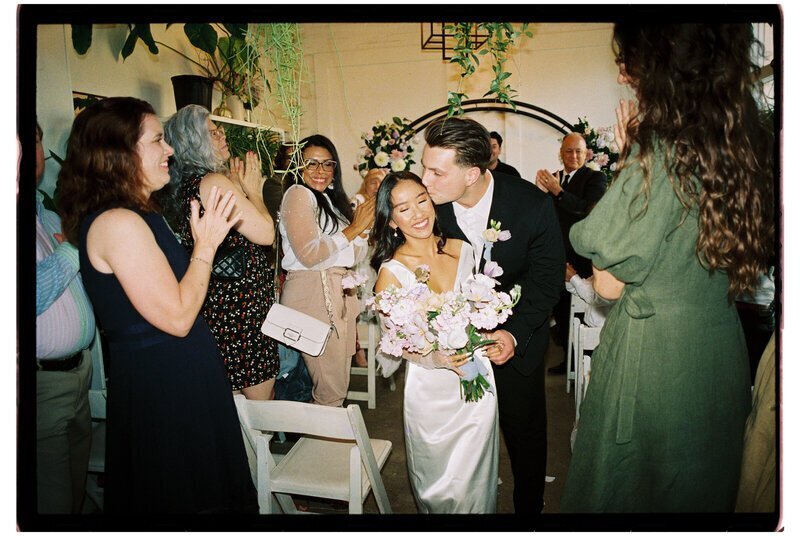 Bride and groom kissing at wedding surrounded by guests in Florida by wedding film photographer Noble Photo Co