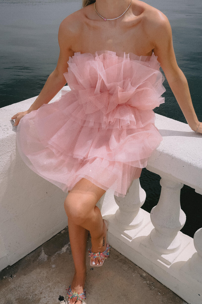 girl sitting on water's edge wearing a pink tool dress