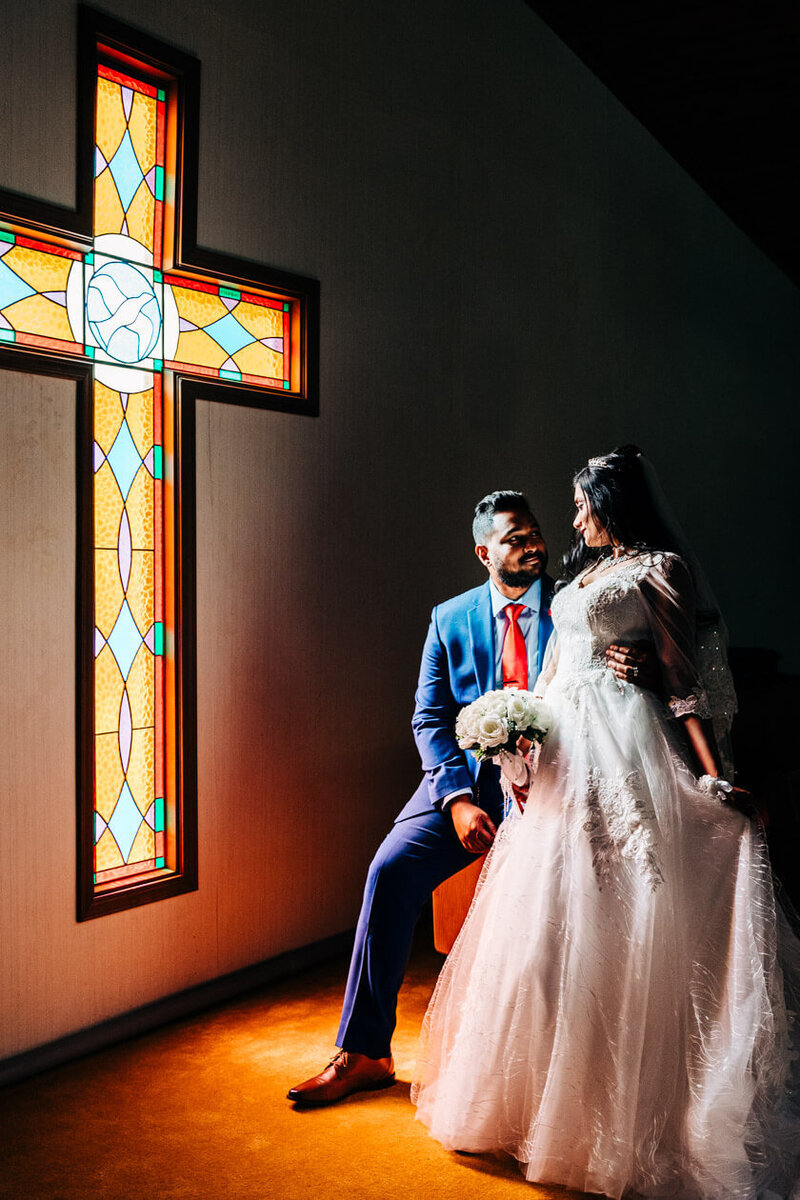 An Indian wedding couple poses together by a cross window at sunset in Indianapolis. Indiana.