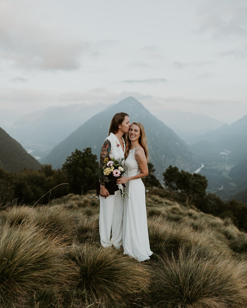a couple in wedding attire kiss at sunrise in front of the Hintersee in the German Alps