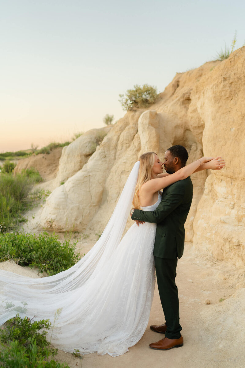 bride leans into her husband in a hug on her husband in the soft sunset light