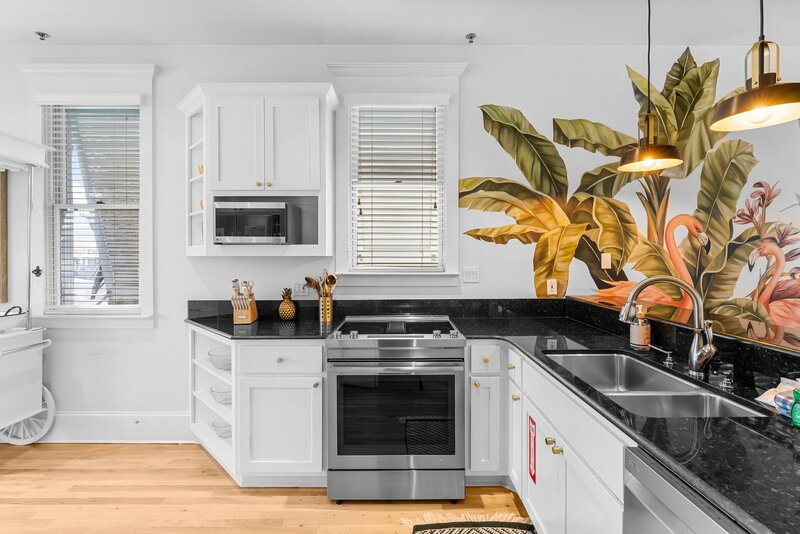 Chic coastal kitchen with colorful flamingo mural and black granite countertops at The Florida House, minutes from 30A beachfront rentals and Santa Rosa Beach vacation homes.