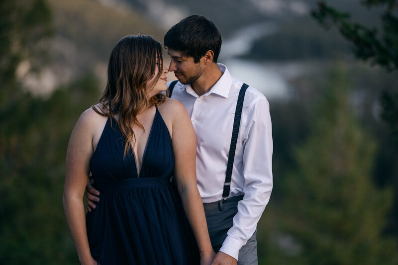 Capture the joyous moment of a couple popping champagne and celebrating their new engagement on top of a mountain after a hiking adventure. A thrilling and romantic scene set against the breathtaking backdrop of the Rockies.