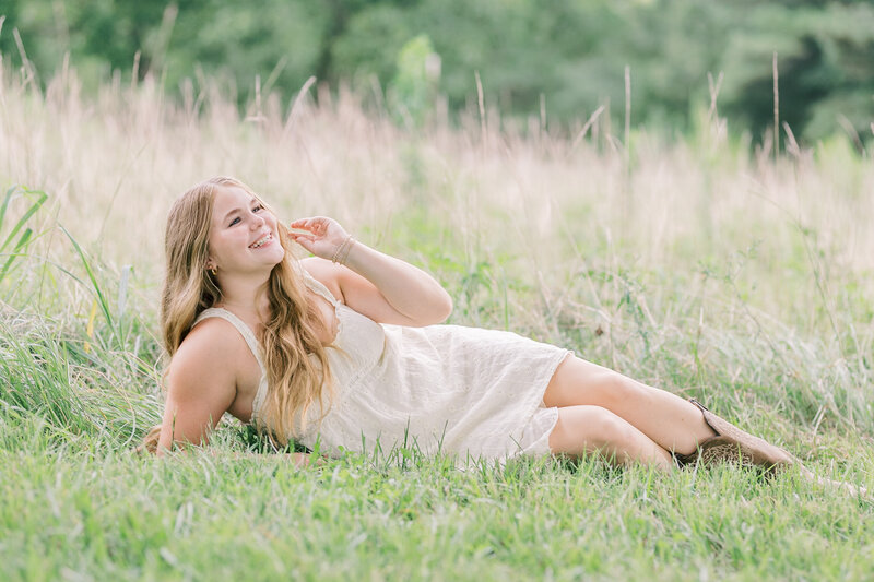 Senior girl laughing while lying in a grassy field during a golden-hour session with Raleigh Senior Photographer Lindsey Lambert Photography.
