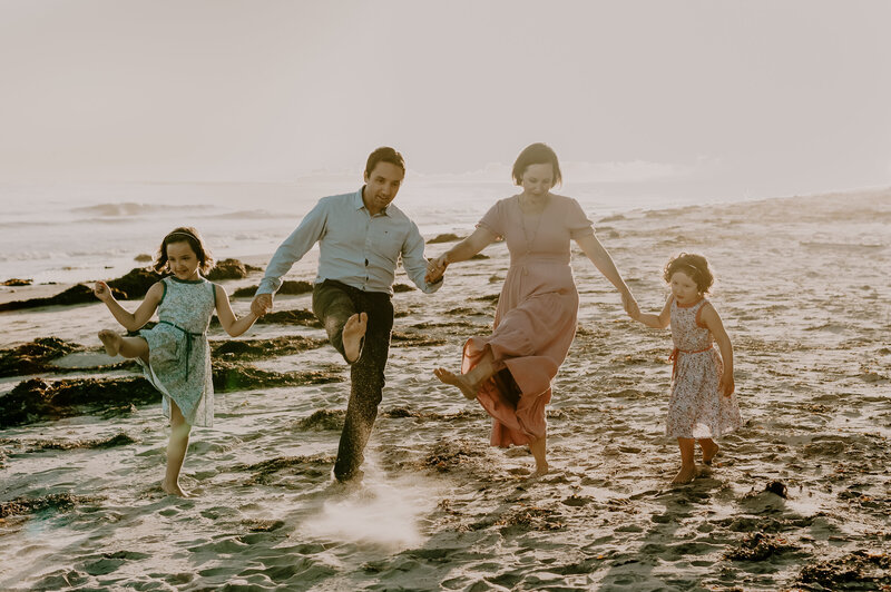 Family walking on beach and kicking their legs up in the air.