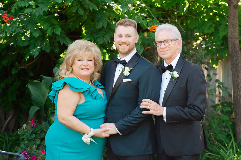 a groom smiling and standing between his mother and father.  Captured outdoors by Ottawa wedding photographer JEMMAN Photography