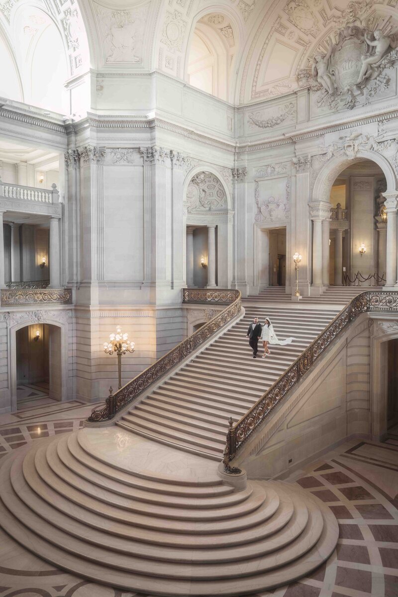 A newlywed bride and groom edcending the staircase in the San Fransisco court house