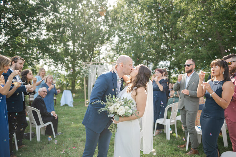 Les mariés s’embrassent à la sortie de la cérémonie dans un mariage rustique et champêtre en Montérégie, moment vibrant de joie capturé dans un décor naturel et chaleureux