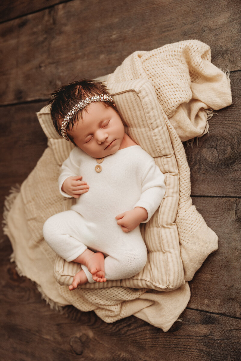 infant posing for newborn portraits in white outfit on soft bedding for newborn portrait session