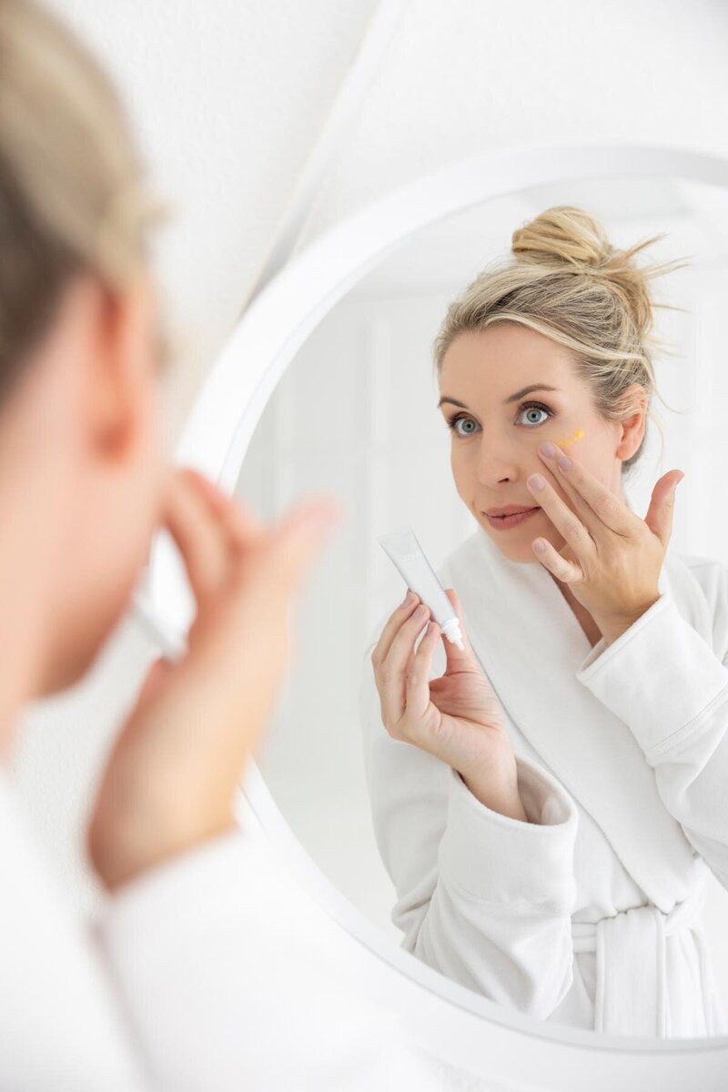 Dr. Maren Locke, board-certified dermatologist, applying anti-aging skincare in front of a mirror as part of her expert-recommended morning routine.