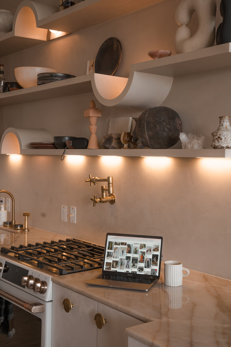 Luxe, upgraded farmhouse kitchen lit with dim lights and a Mac Book Pro laptop on the counter between the stove and mug