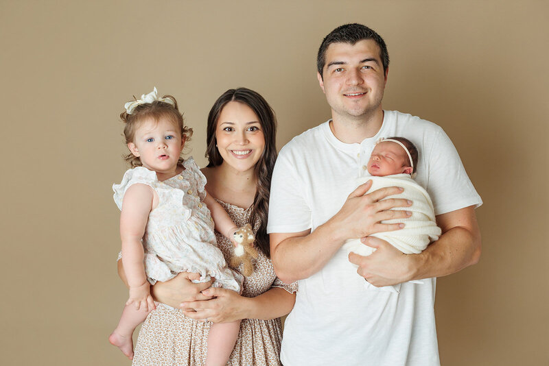 A serene newborn baby is sleeping, wrapped snugly in a soft, neutral-toned fabric. The baby has closed eyes and a calm expression, lying against a gentle, textured backdrop that enhances the cozy atmosphere.