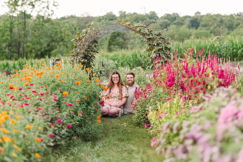 couple sitting in the grass between rows of colorful flowers mini session country joy flowers lancaster pa photographer