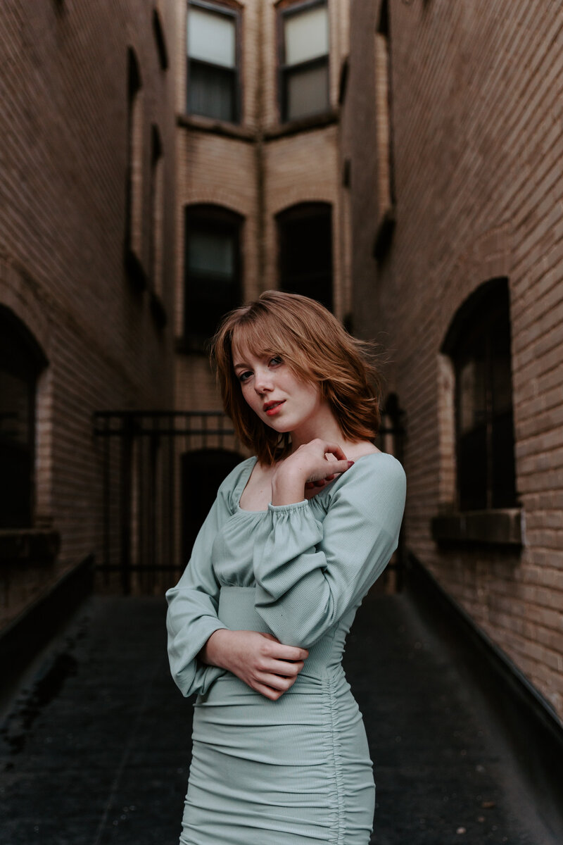 A person standing in an alleyway with one arm on her shoulder
