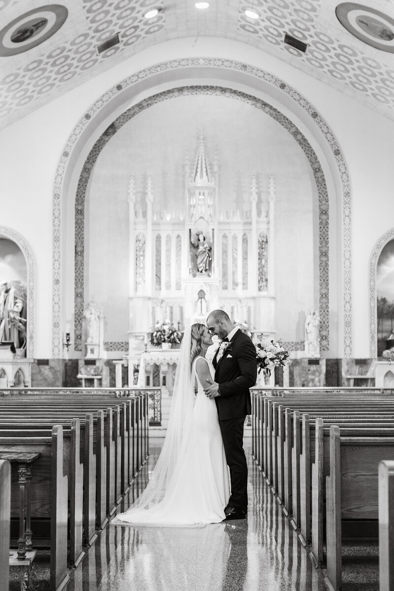 Black and White image of a couple standing in a church. Their foreheads are touching.