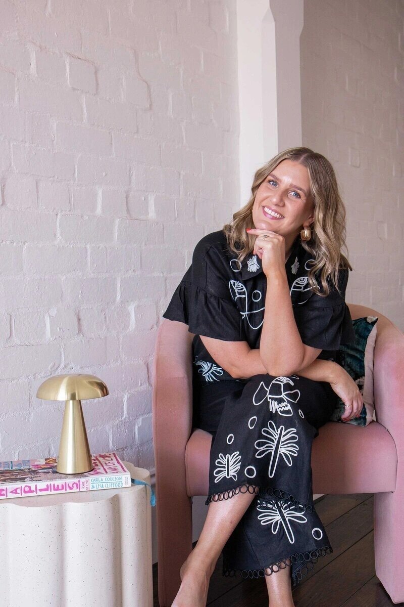 Photo of Nikki Weedon sitting on a couch against a white wall while smiling