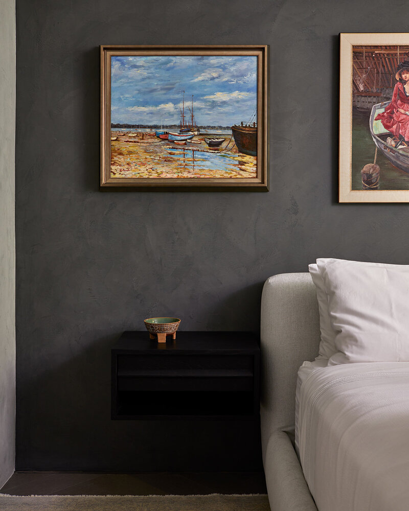 A floating black bedside table mounted to a dark grey wall and surrounded by framed paintings