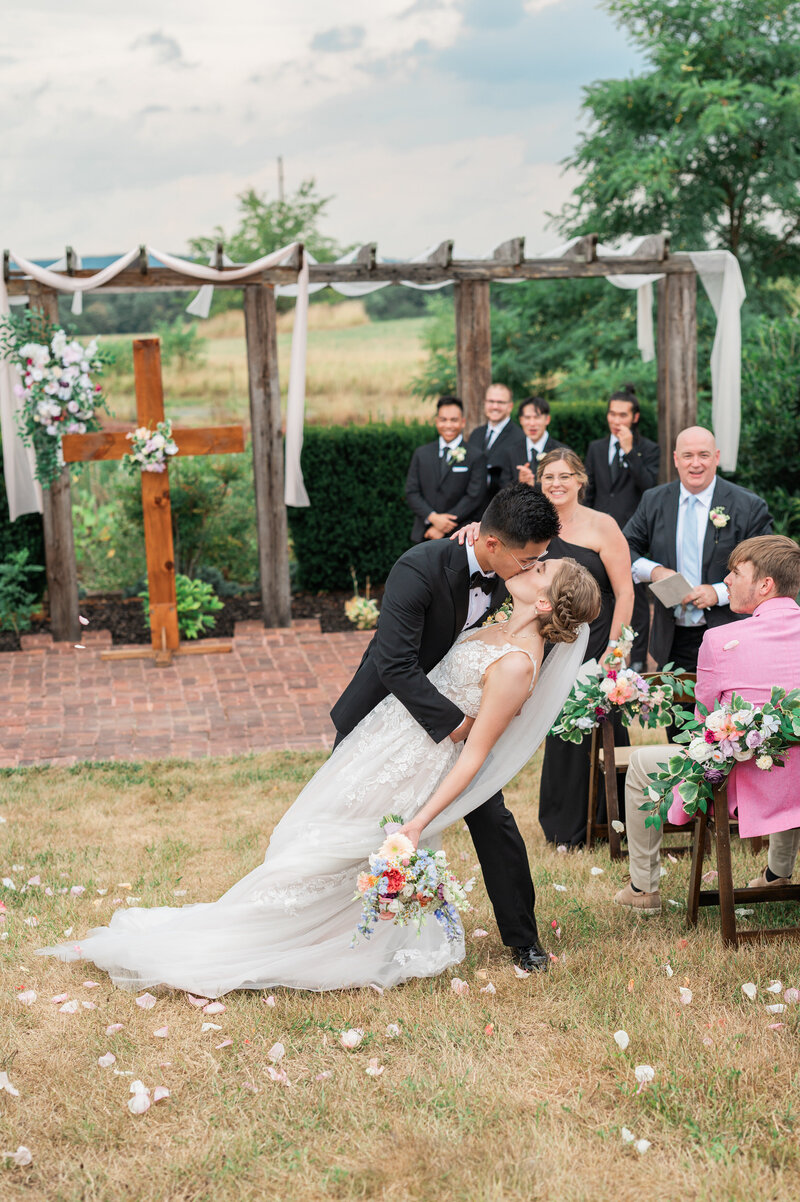 A person dipping their partner in the middle of the aisle and kissing them after their wedding ceremony