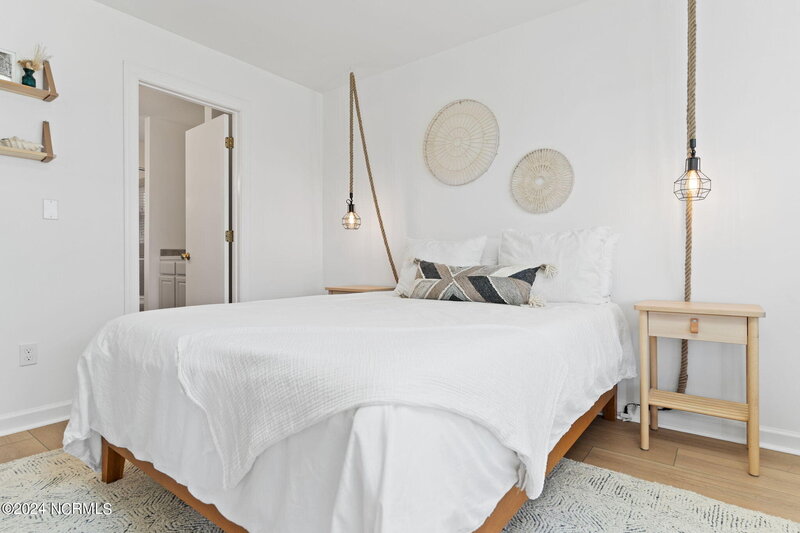 Owner’s master bedroom with cherry wood bed frame, crisp white linens, woven basket wall art, industrial hanging light, and light wood nightstand.