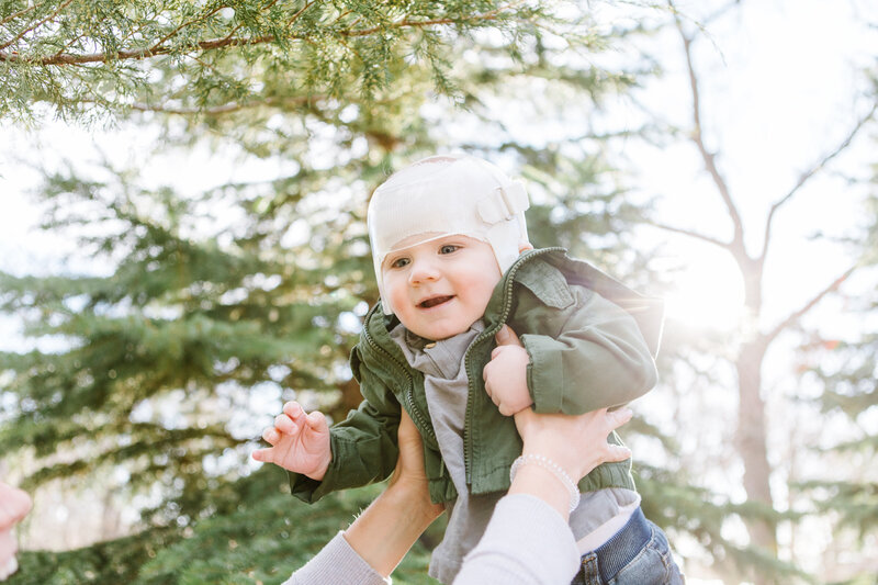 A mother lifting her baby high, with the baby wearing a Cranial Remolding Orthosis (pediatric helmet).