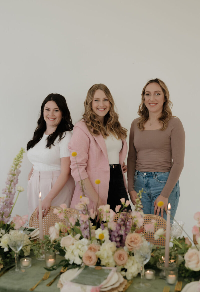 Liz, CJ, &  Molly, Dream Weddings Wisconsin Wedding Planner Team for Dream Weddings, standing around a floral designed table in Milwaukee smiling at the camera.