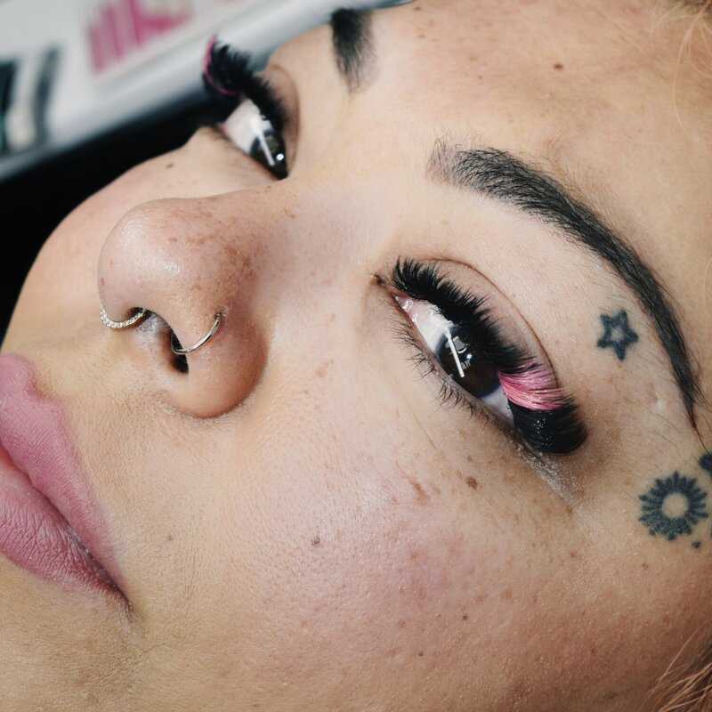 Close-up of pink lash extensions on a tattooed client with a bold personal style.