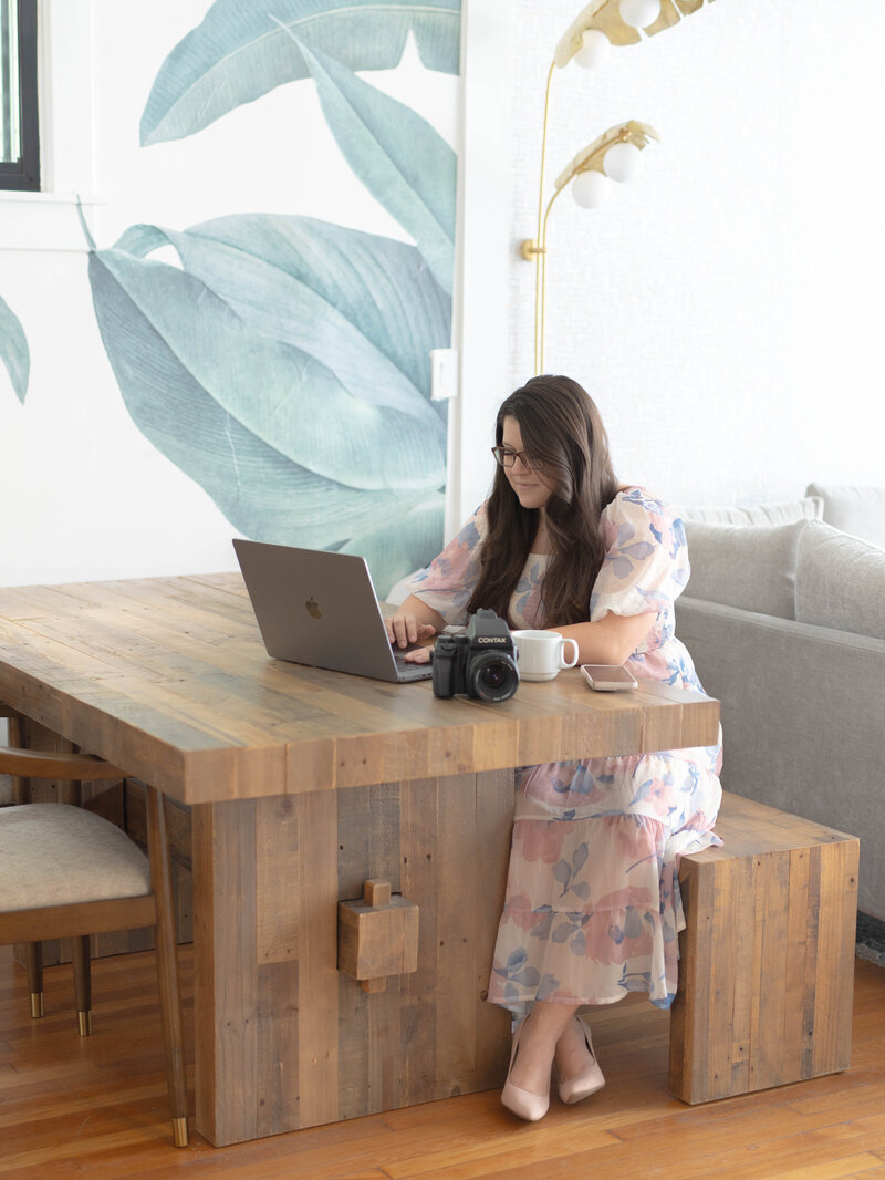Photographer typing on her laptop with camera next to laptop