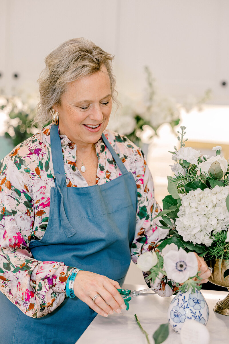 Blonde woman in apron smiling while cutting flowers