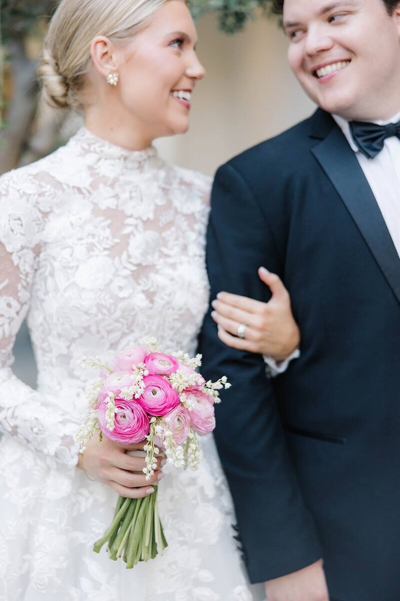 Bride and groom with their arms interlocked smiling at each other in front of a brick wall