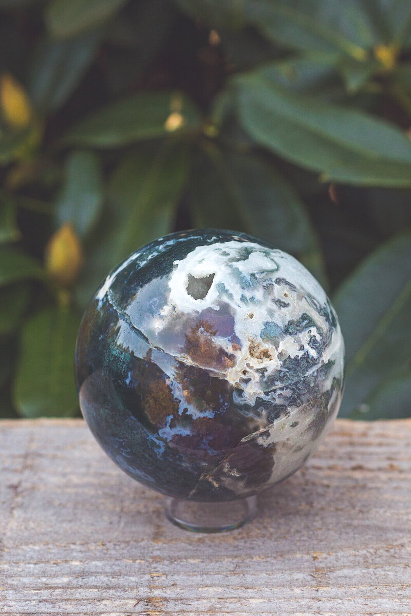 The other side of a moss agate sphere crystal with deep teal, blue, and green colours.