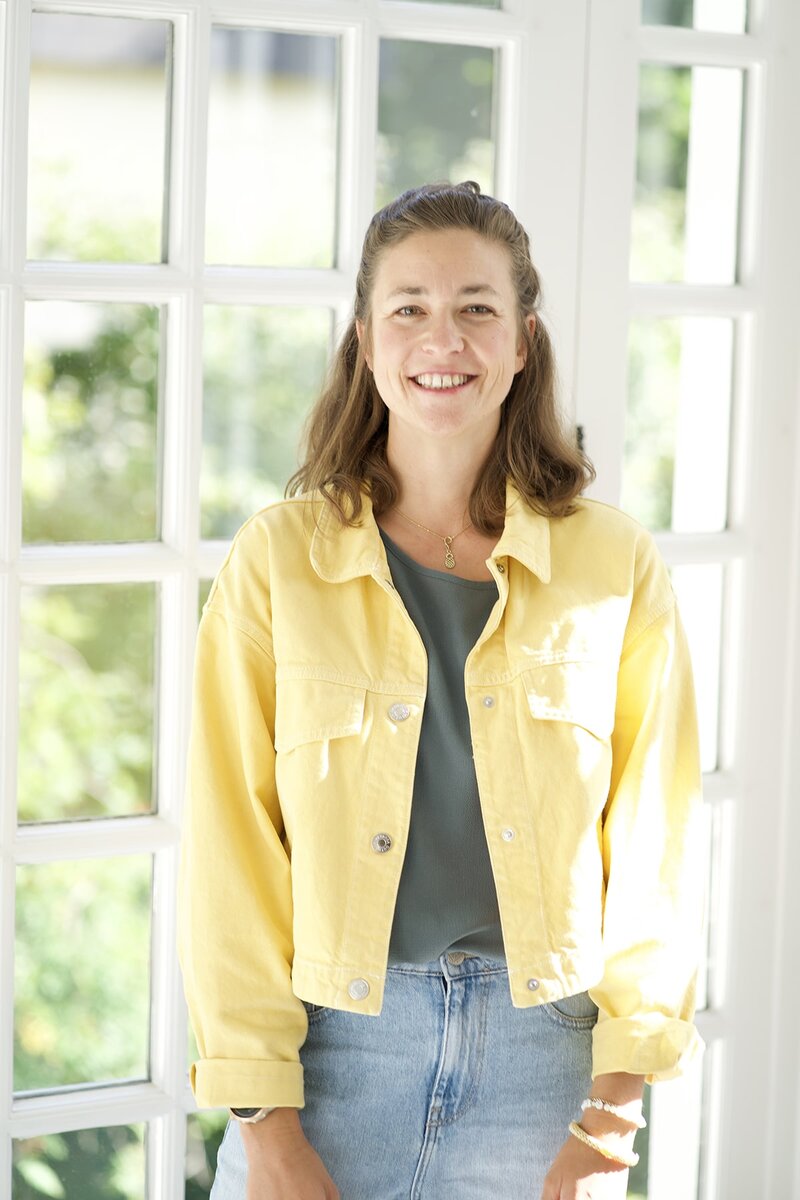 Portrait von Hanna Zöller in gelber Jacke, Eventmoderatorin und Innovationsmanagerin aus München, sympathisch lächelnd am Fenster
