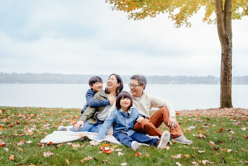Family sitting together among vibrant fall foliage at O.O. Denny Park, surrounded by golden autumn colors.