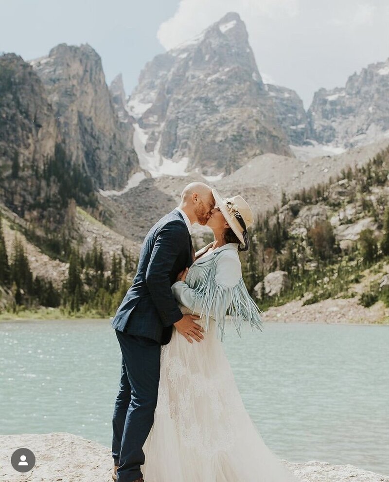 Grand Teton National Park elopement photographer Adriana Montoya Photo. A groom is kissing his bride with a bright blue lake and stunning mountains behind them.
