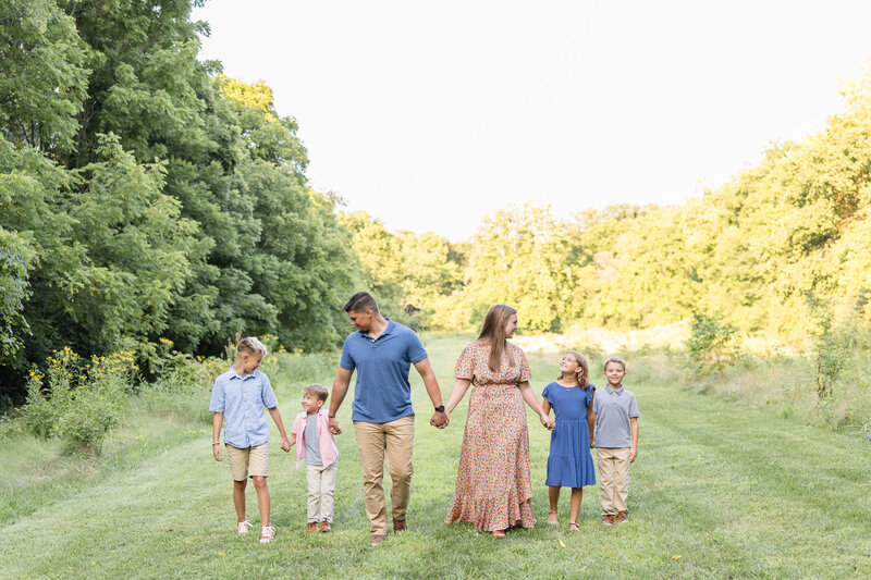 Family of six holding hands in a line walking towards the camera smiling and joyfully laughing at each other.