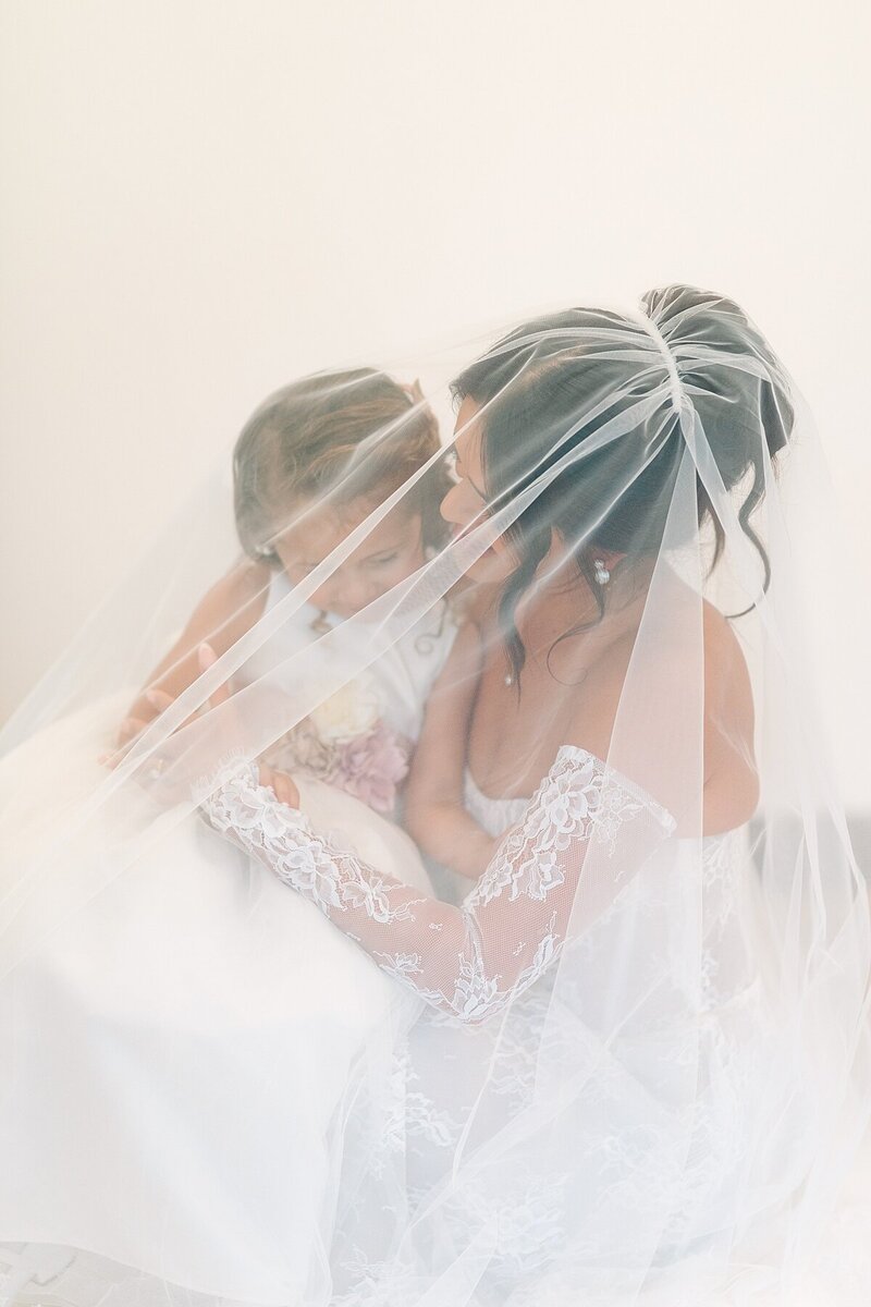 Bride holding her niece and flower girl under her veil before walking out for the ceremony at Rancho Guijito Vineyard in Escondido.
