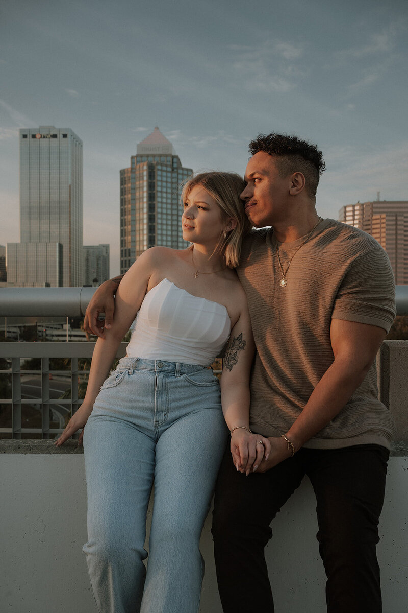 couple holding hands with city skyline during engagement session golden hour