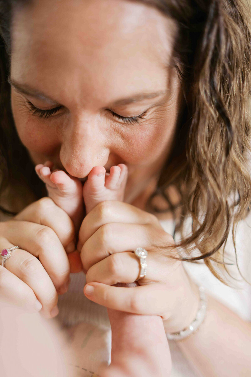 Mother sitting on yellow sofa with yellow damask curtains sitting on couch while gently rubbing newborn baby on the head laying next to her  by Portland Family Photographer Emilie Phillipson Photography. 
