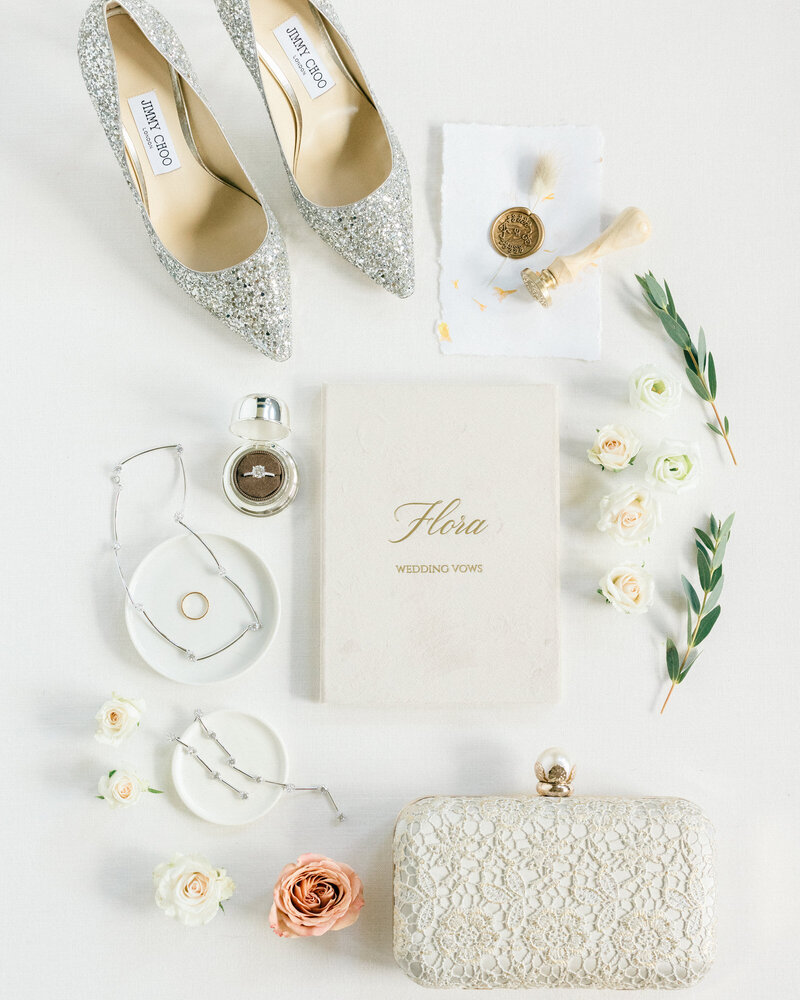 Flat lay photograph of bridal wedding day details including the bag, earrings, rings and shoes arranged together for an elegant and stylish detail image captured by editorial wedding photographer Geoff Wilkings