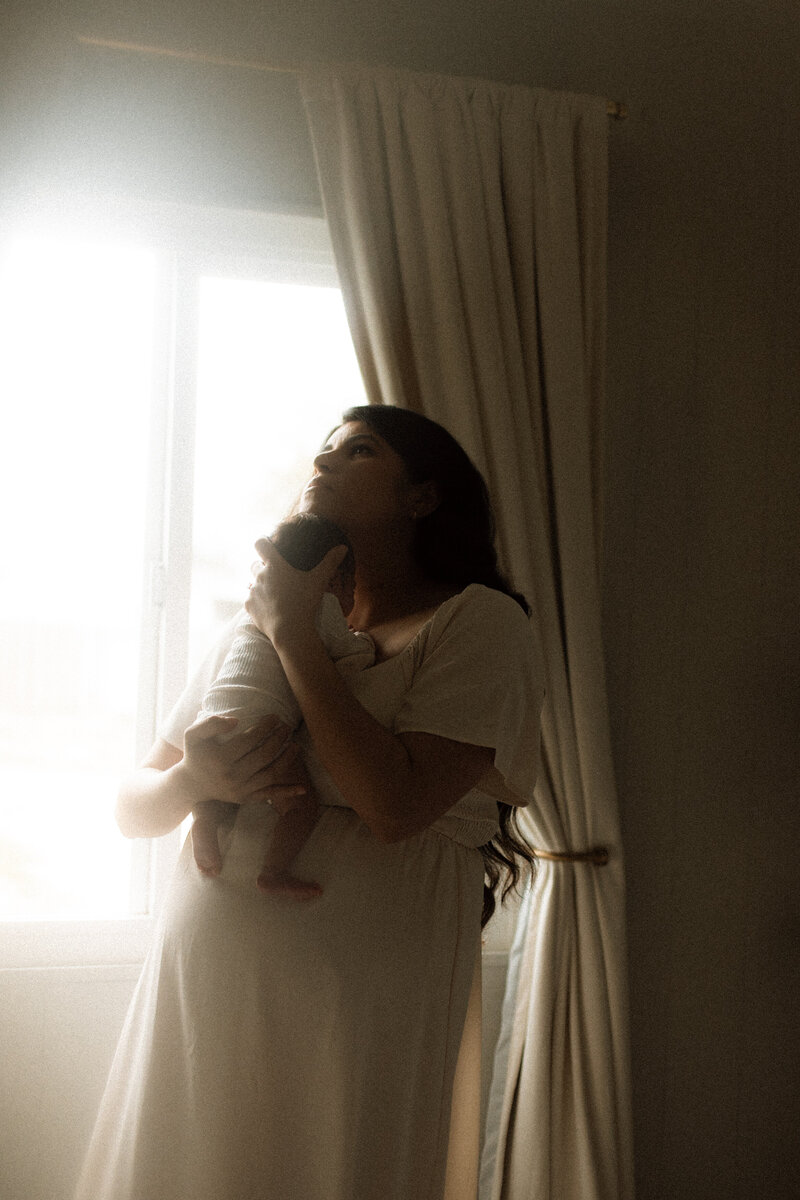 New mom holding her baby close, eyes closed, in a cozy in-home newborn session in Murrieta.