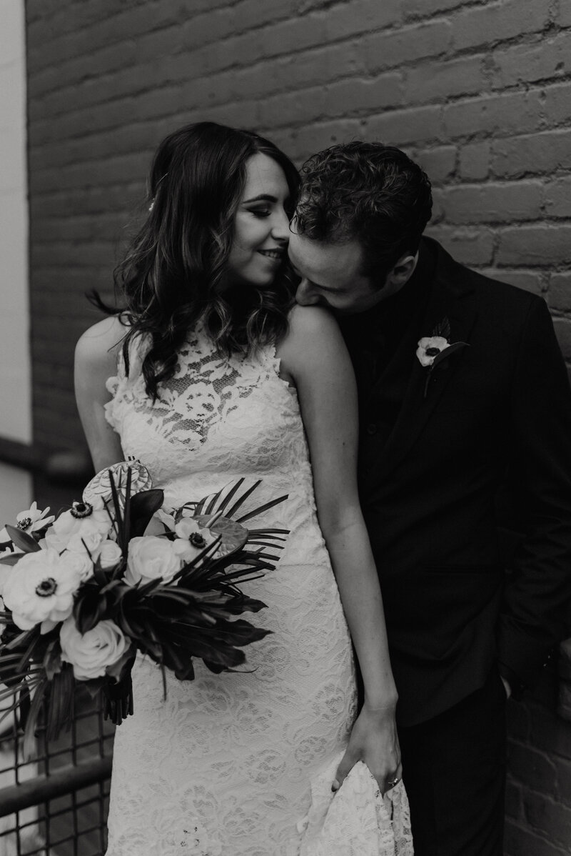 A groom kissing his bride's cheek while she closes her eyes and holds her bouquet.