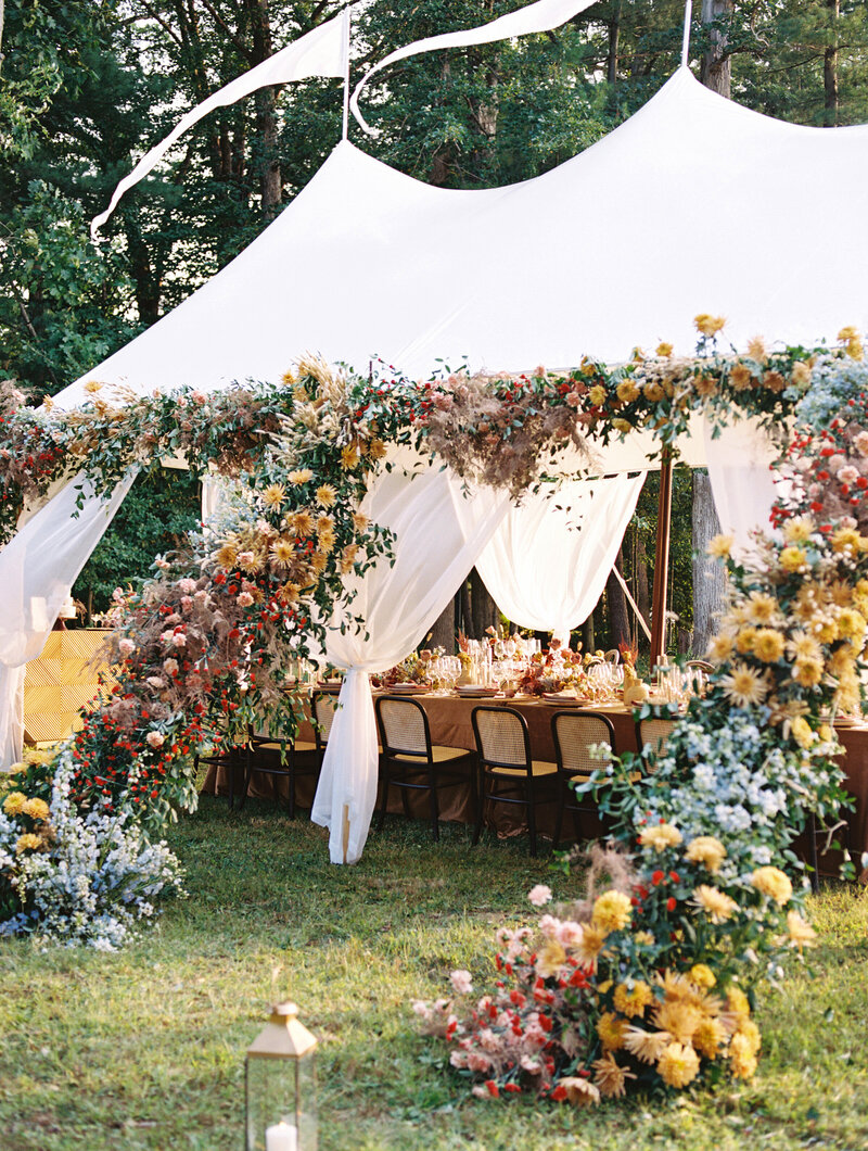 Outdoor wedding tent adorned with colorful floral arrangements and draped white fabric.