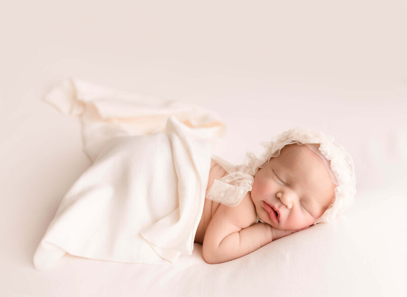 Newborn Baby girl on Cream posted with headband sleeping