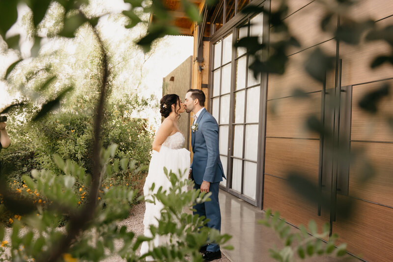 bride and groom kissing outside of building