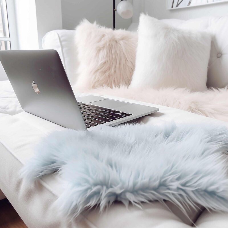 Feminine workspace with silver laptop on a soft faux fur throw and blush pillows — representing cozy, aesthetic blogging setup for women launching profitable blogs with coaching support

